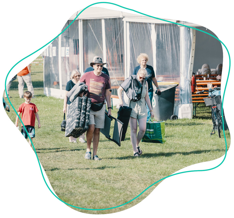 Festivalbesucher tragen ihre Ausrüstung über das Gelände des WDL-Dünenhofs und freuen sich auf gemeinsame Tage.