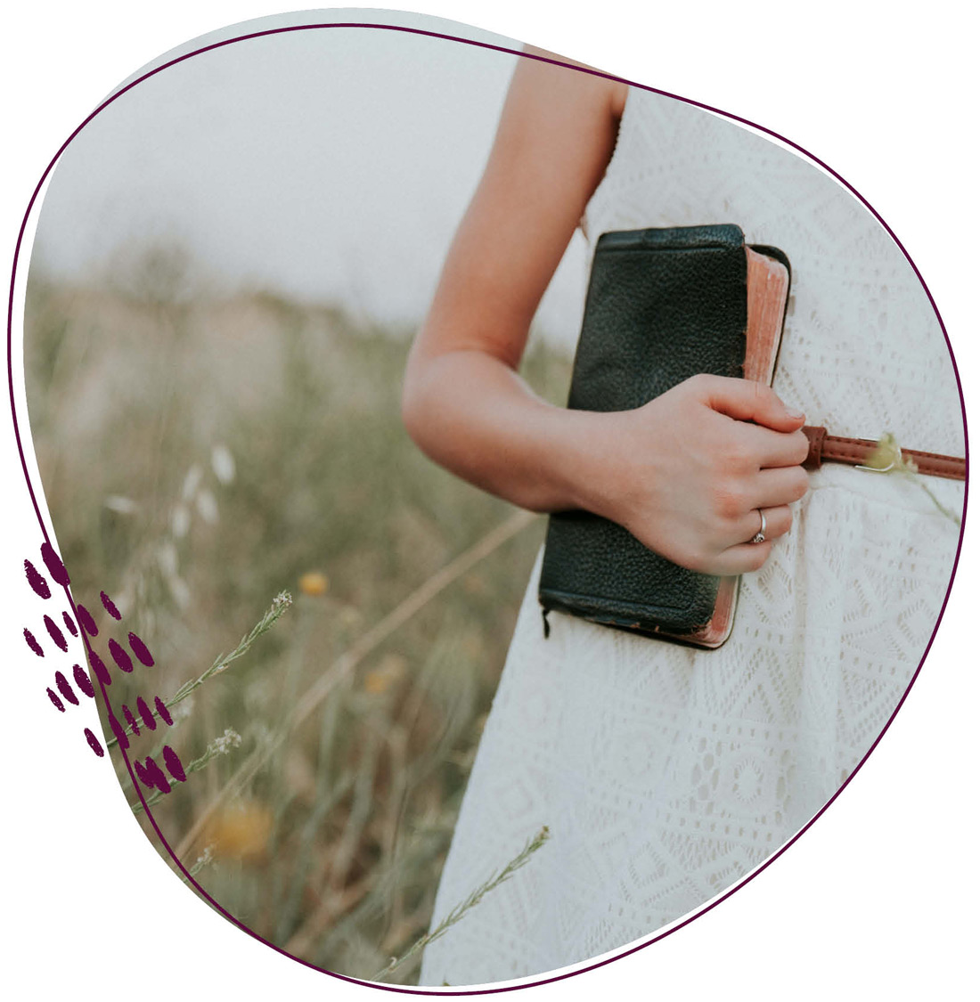 Eine Frau hält eine Bibel in der Hand und steht inmitten einer natürlichen Wiesenlandschaft 