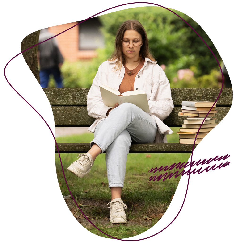 Ein Mädchen sitzt nachdenklich mit einem Buch auf der Bank und liest beim einem Kurzwochenseminar beim WDL Dünenhof