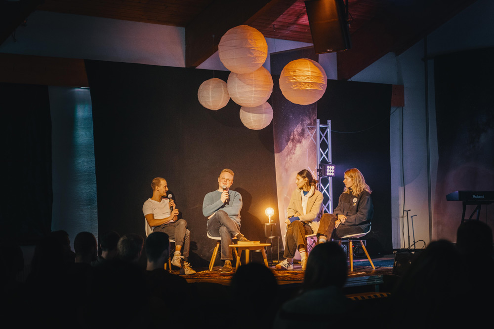 Vier Personen sitzen in einer Runde auf einer Bühne und diskutieren miteinander 