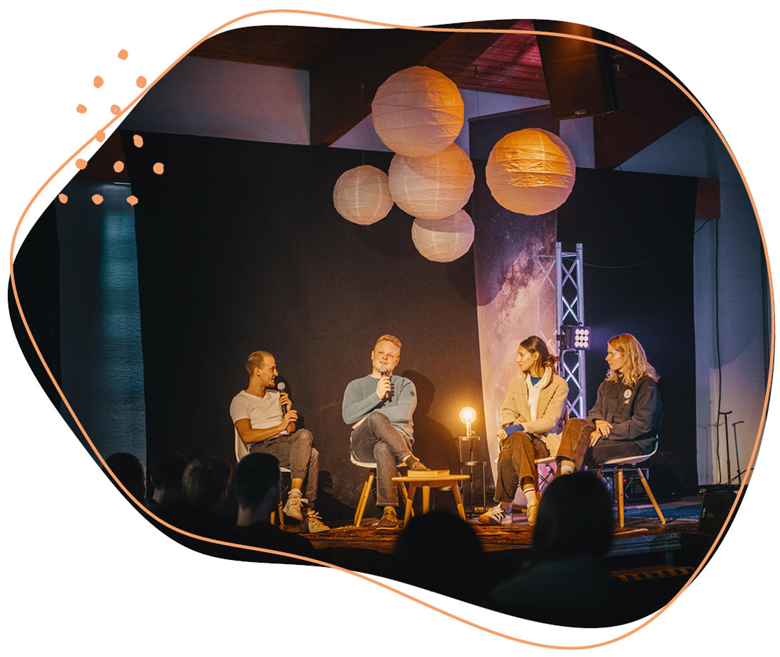 Vier Personen sitzen in einer Runde auf einer Bühne und diskutieren miteinander 