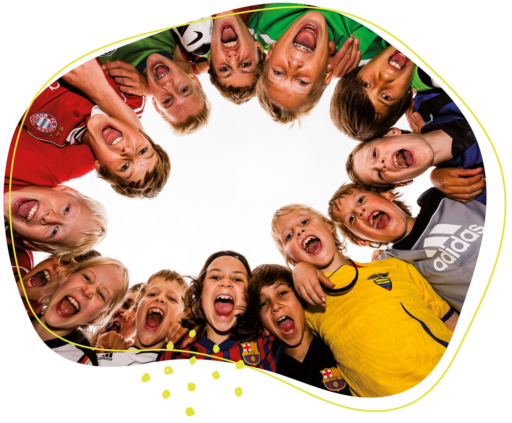 Eine fröhliche Gruppe von Kindern in bunten Fußballtrikots steht eng im Kreis zusammen und jubelt ausgelassen in die Kamera.