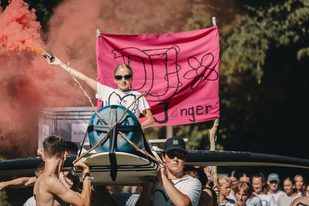  Eine junge Frau hält eine Flagge und ein Rauchsignal auf einem Auto, umgeben von einer Menschenmenge.