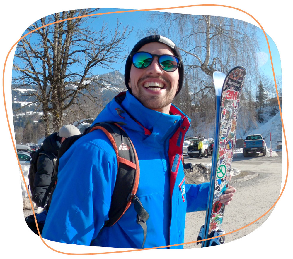 Mann der in die Kamera lächelt und Skier in der Hand hat