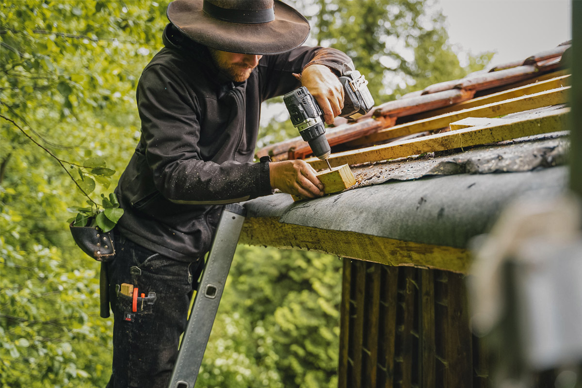 Mann der auf einer Leiter steht und ein Dach deckt